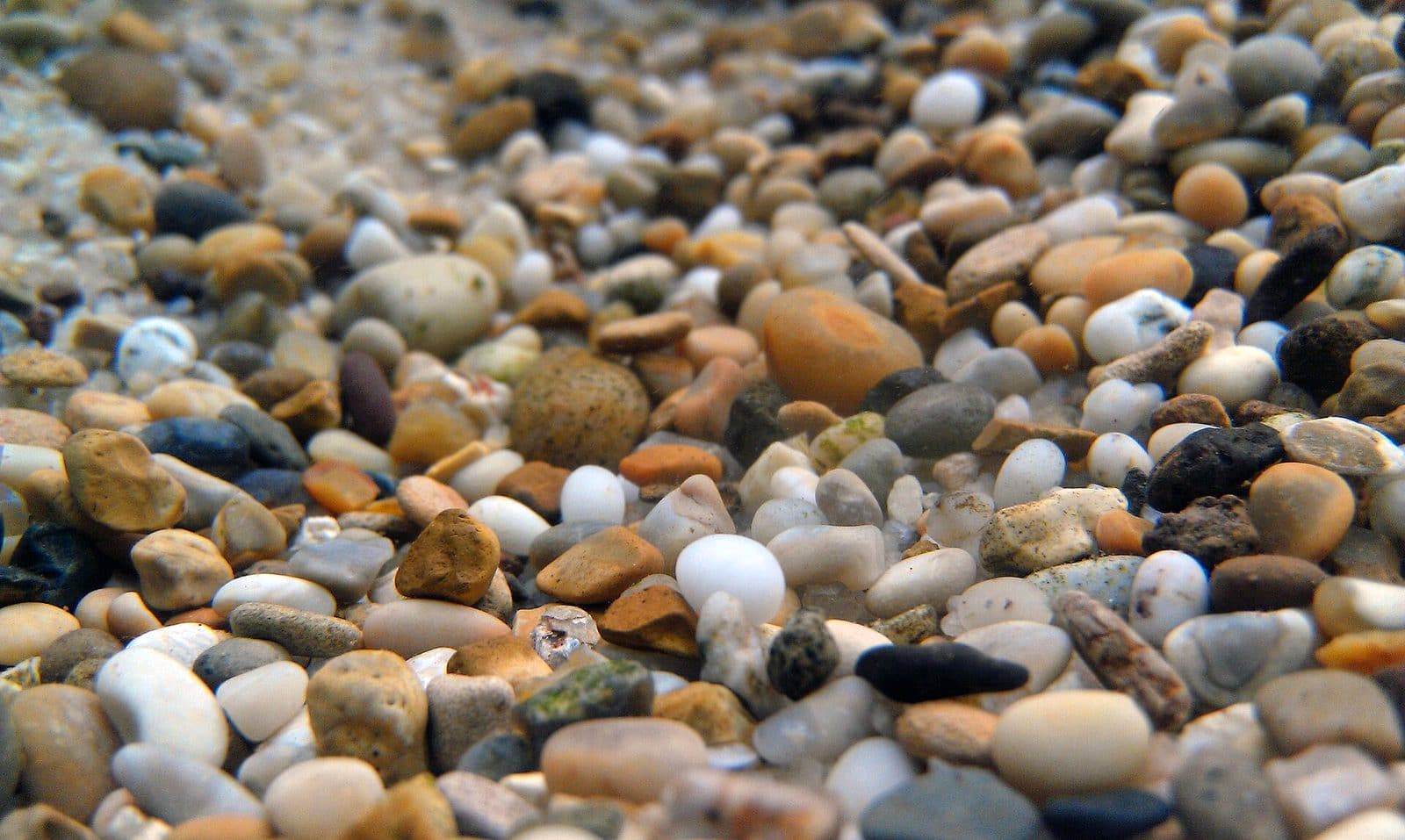 Close view of a bed of mixed brown, cream and grey aquarium gravel, with rounded pebbles of varying size filling the frame.