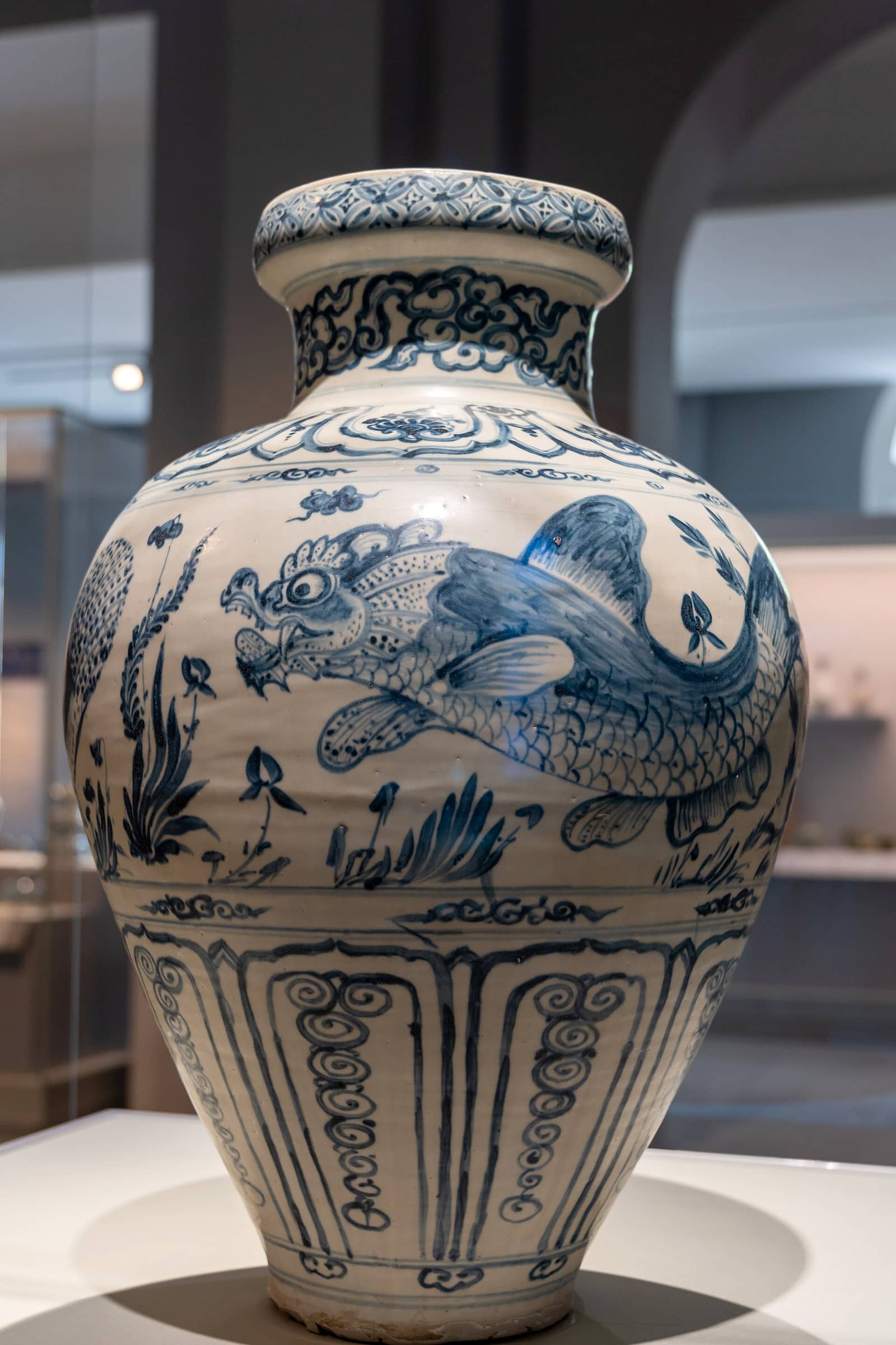 A blue-and-white stoneware jar from 14th-15th century Vietnam decorated with painted fish, displayed in a museum case.